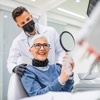 Woman in dental chair smiling with dentist behind her touching her shoulders