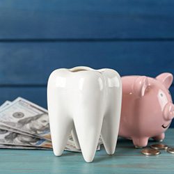 Giant plastic tooth next to a piggy bank and dollar bills