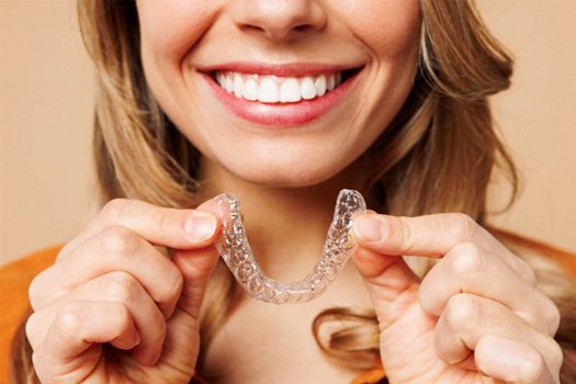 Nose-to-shoulder view of woman smiling holding Invisalign tray