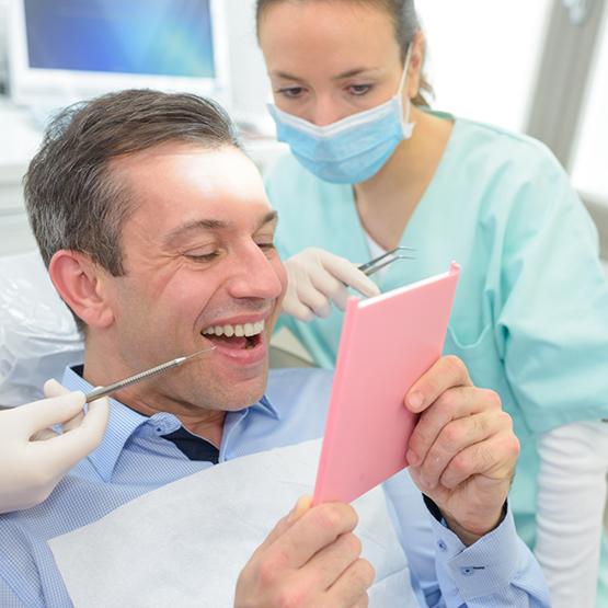 Man in dental chair looking at his smile in mirror