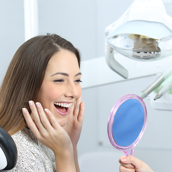 Dental patient beaming at her new smile in mirror