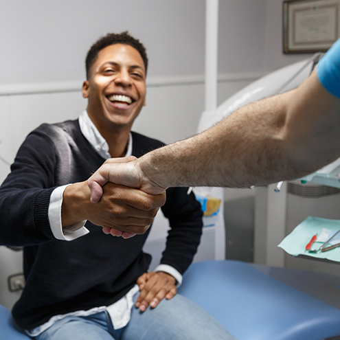 Smiling man in dental chair shaking hands with his Reno dentist