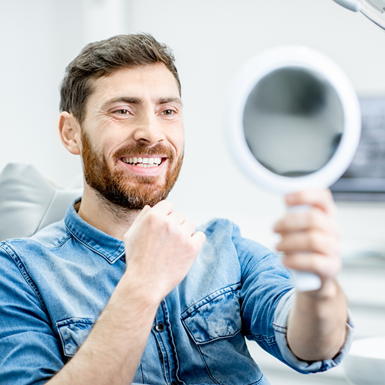 Man in dental chair admiring his smile in mirror