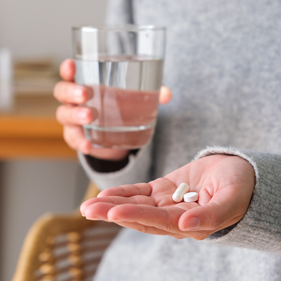 Person holding a glass of water in one hand and a few pills in the other