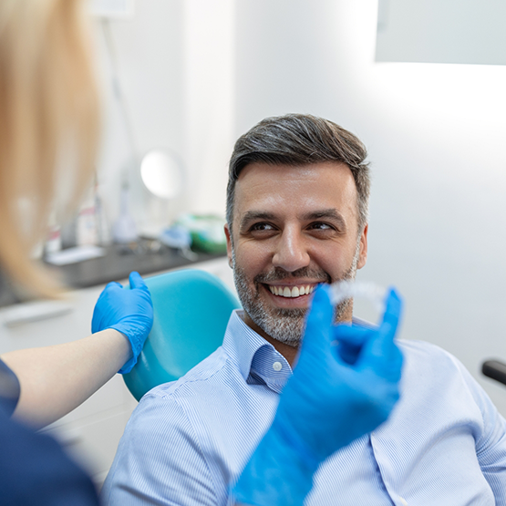 Man smiling at his dentist who is holding a clear aligner