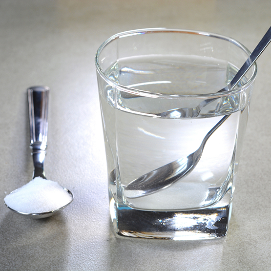 Spoonful of salt on table next to glass of water